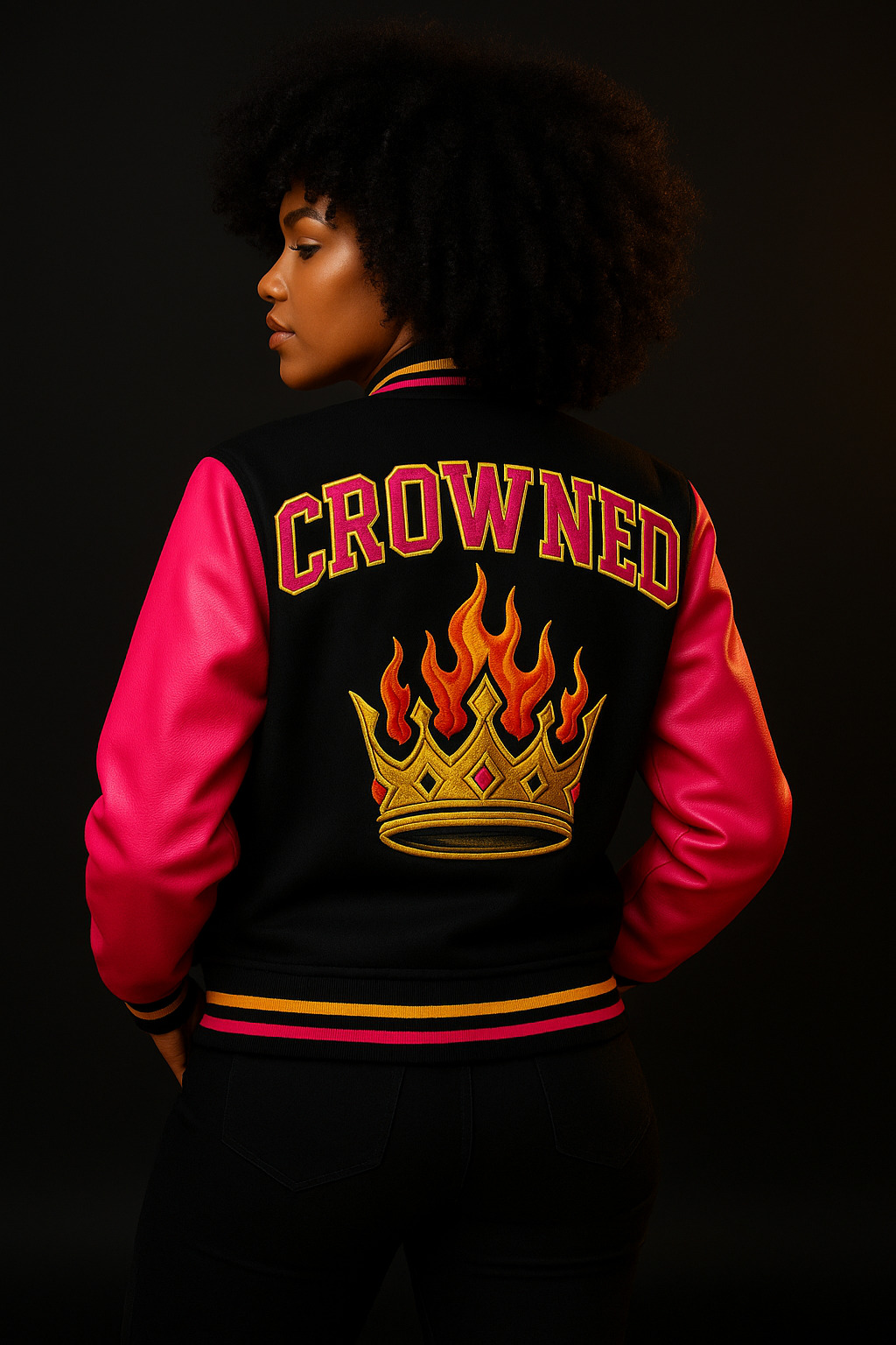 High-resolution photograph of a sleek black bomber jacket with Crowned By Fire embroidery, displayed against a dark backdrop with glowing gold accents, representing the “Armor of Ashé” jackets collection.